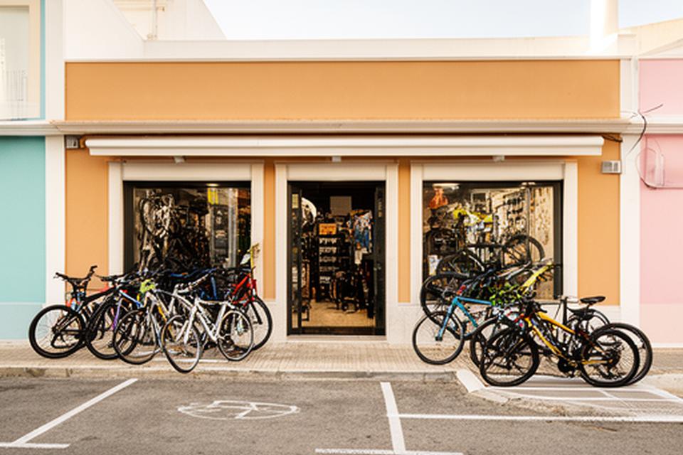 Fachada da loja de bicicletas em Estômbar e Parchal com bicicletas expostas e estacionamento junto à estrada